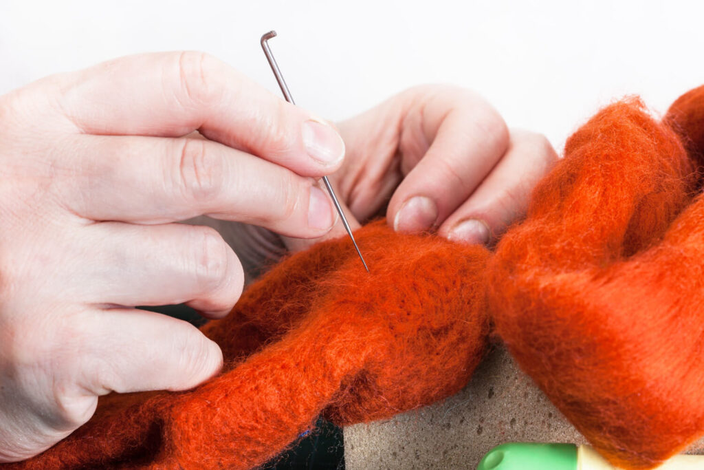 Hands felting orange wool with needle.