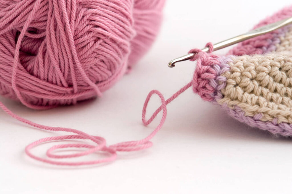 Pink yarn ball, crochet hook, and crocheted fabric. Pink and beige yarn.