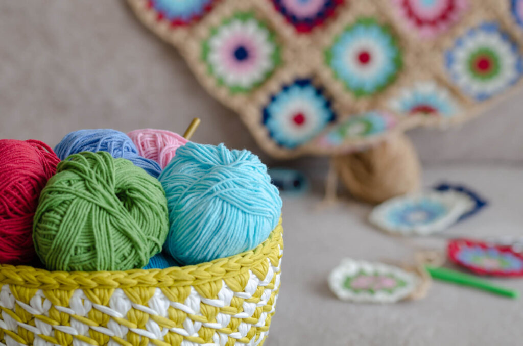 Colorful yarn balls in a crochet basket. Crocheted items in the background.