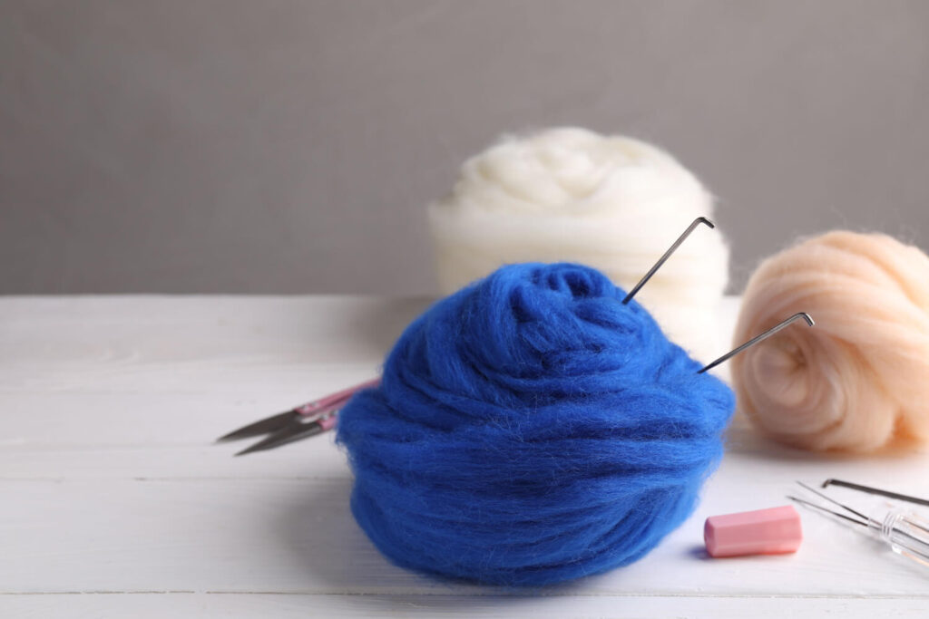 Blue, white, and beige wool roving balls with needles, tools for felting.