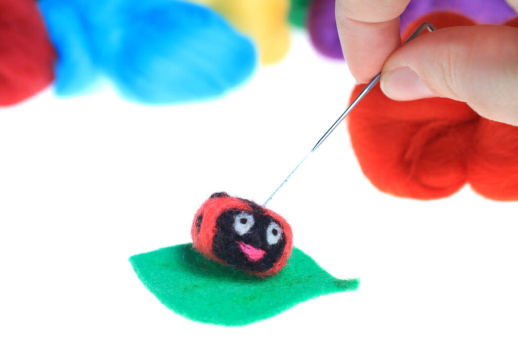 Handmade felt ladybug on green leaf, needlework.