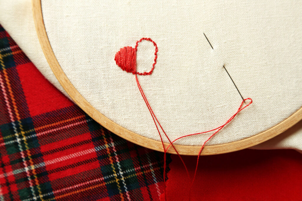 Small red heart embroidery on cream-colored fabric, in embroidery hoop.