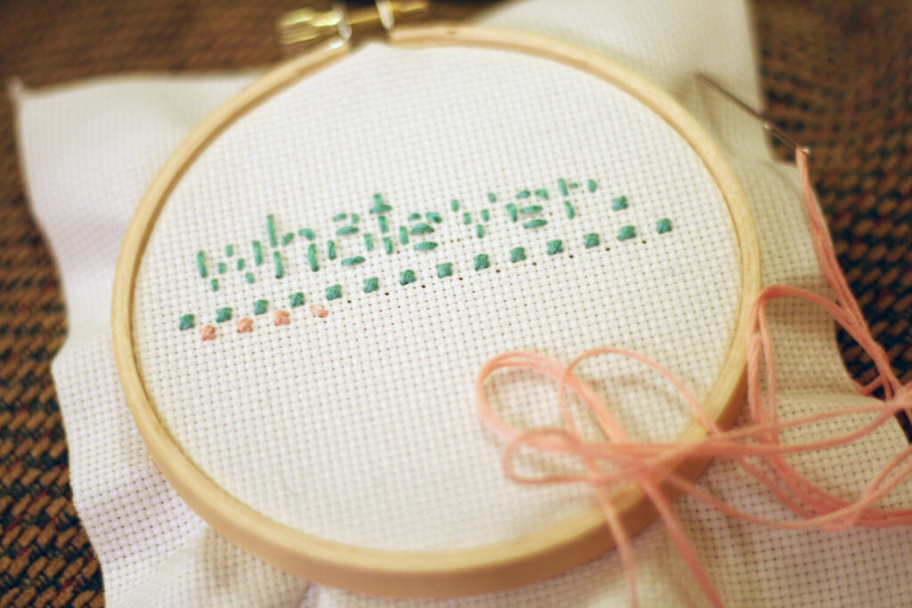 Close-up of a cross-stitch hoop, light beige fabric, green embroidery on a light beige background.