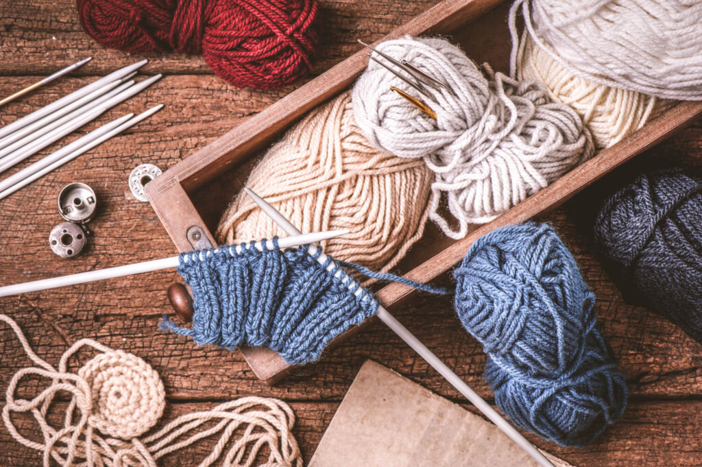 Knitting supplies on wooden table: yarn balls, needles, and knitted fabric.